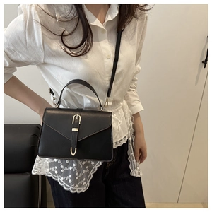 Detail of a black leather crossbody bag with a gold buckle and adjustable strap