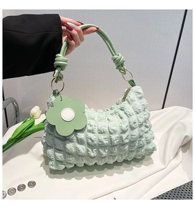 Detail of light green pleated handbag featuring knotted handle and floral charm accessory