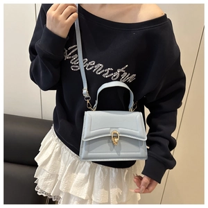 Detail of light blue structured leather handbag with gold chain buckle and top handle