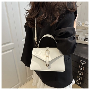 Detail of white leather envelope handbag featuring a golden buckle and slim strap