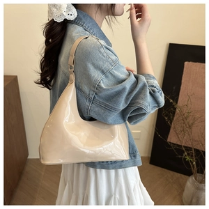 Side view of beige patent leather hobo bag worn by a model in a minimalist room