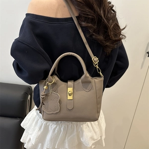 Sac seau en cuir taupe avec fermoir doré et breloque chien porté par un mannequin