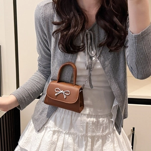Sac bandoulière chic en cuir marron avec nœud argenté et chaîne porté par un mannequin