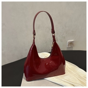 Detail view of burgundy patent leather hobo bag with gold zipper on textured surface