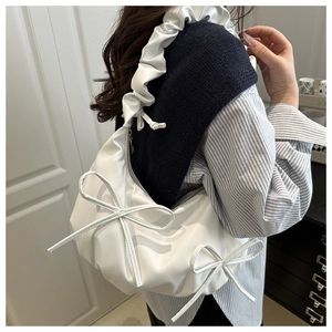 Close-up of a white pleated shoulder bag featuring elegant side bow details and a scrunchie strap
