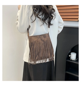 Détail d'un sac bandoulière en daim marron foncé avec de longues franges et métal doré