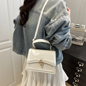 White faux leather crossbody bag with gold lock buckle and top handle shown on a model