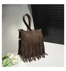 Détail d'un sac hobo en daim marron avec franges et poignée simple sur surface blanche
