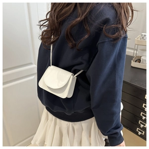 Detail of a white minimalist PU leather crossbody bag worn by a model in a casual setting