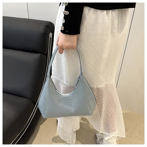 Detail of light blue leather hobo bag with zip closure held by a model in a modern room