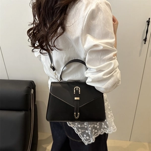 Elegant black faux leather crossbody handbag with gold buckle in minimalist home setting