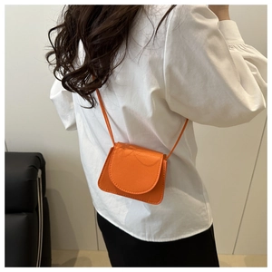 Detail of bright orange lychee textured mini crossbody bag worn by a model in lifestyle view