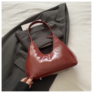 Close-up of dark red patent leather shoulder bag with metal studs on white textured background