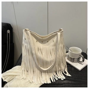 Détail d'un sac à franges crème avec œillets dorés posé sur une table en bois noir
