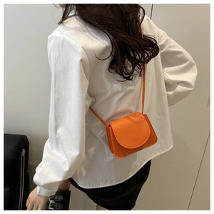Back view of a small orange crossbody bag with litchi grain texture on a female model