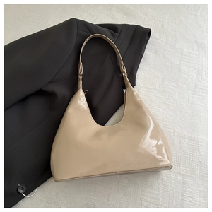 Detailed close-up of a beige glossy patent leather hobo bag on a black blazer backdrop