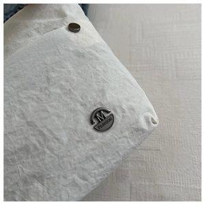 Detailed close-up of textured nylon fabric with M FASHION metal logo and dark grey hardware