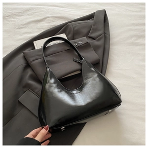Close-up of black patent leather hobo bag with FASHION logo and metallic feet details