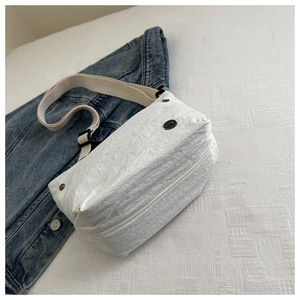 Detail of white crinkled fabric crossbody bag with black metal logo on blue denim