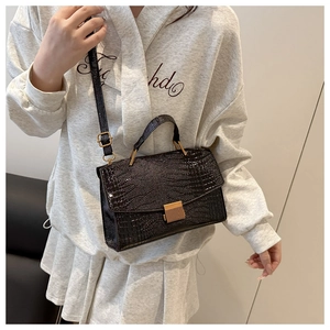 Detail of black crocodile texture handbag with golden vertical lock on a lifestyle model
