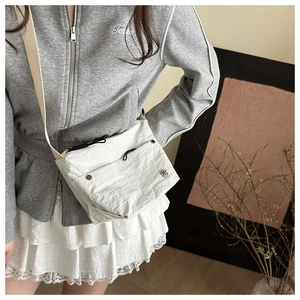 Detail of white nylon crossbody bag featuring pleated texture and silver logo emblem