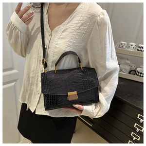 Close-up of black croc-embossed square handbag with golden metallic lock and top handle