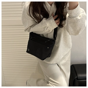Detail of a black nylon crossbody bag with a metal logo and adjustable wide strap