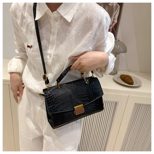 Detail of black crocodile texture bag featuring gold vertical clasp and polished handle