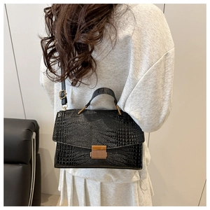 Detail of a black faux-crocodile leather handbag worn by a model in a casual setting