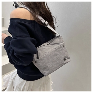 Close-up of a light grey nylon crossbody bag on a model featuring fine metal hardware
