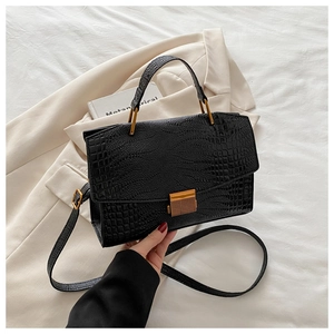 Close-up of black crocodile embossed texture and golden metal push lock on handbag