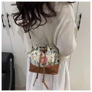 Schicke geblümte Eimertasche mit Kordelzug am Modell in weißem Interieur präsentiert