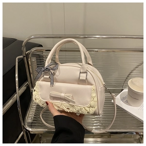 Detail of cream white lace-stitched bag with bow handle and magnetic pocket