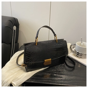 Detail of black crocodile texture handbag with gold metal clasp and leather strap