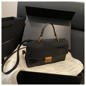 Detail view of a black crocodile-pattern handbag with elegant gold metal clasp in a gift box