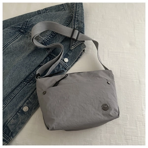 Detail of grey lightweight nylon messenger bag with circular metal logo on denim background