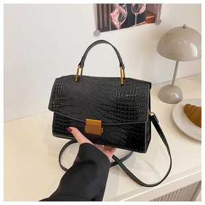 Detail of black crocodile texture handbag with gold metal clasp and detachable strap