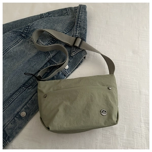 Detail of light green nylon crossbody bag with wide grey strap and metal logo on textured fabric