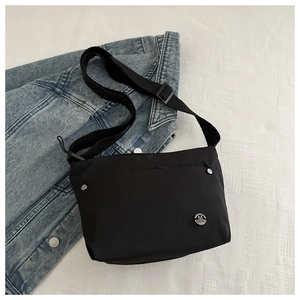 Close-up of black nylon square bag with silver metal M logo on white textured fabric