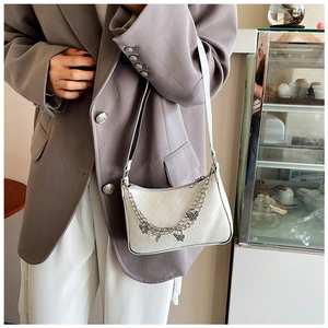 Close-up of white quilted baguette bag with silver butterfly chain and slim strap