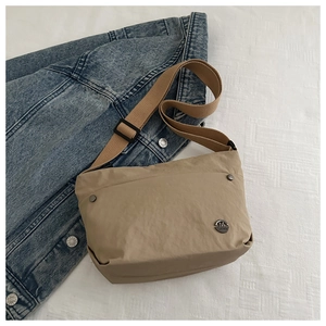 Detail view of khaki nylon crossbody bag with metal logo on denim jacket background