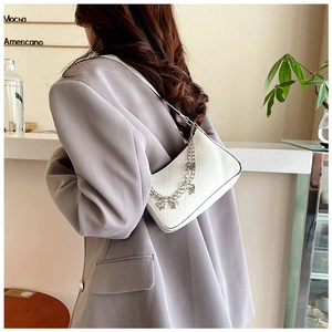 Detailed view of white quilted crossbody bag with silver butterfly chain on model