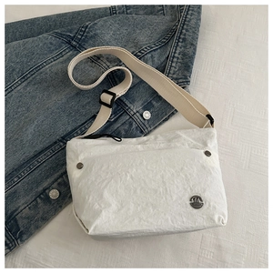 Detail of white wrinkled texture bag with metal M FASHION logo and adjustable canvas strap