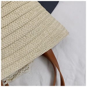Close-up of woven straw bag with brown leather strap and delicate white lace trim details