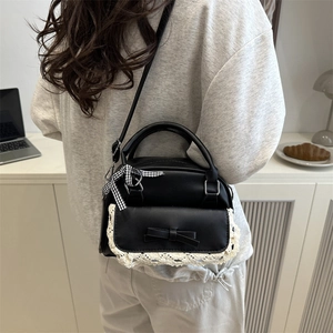 Chic black crossbody bag with white lace trim and bow charm in a cozy lifestyle setting
