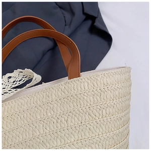 Detail of woven straw tote bag featuring white lace trim and brown leather handles