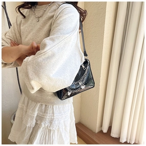 Detail of black glossy patent leather shoulder bag with butterfly silver chain accents
