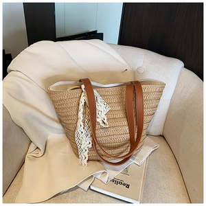 Detail of straw tote bag showing brown leather straps and delicate white lace trim detail