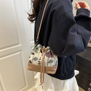 Floral print woven drawstring bucket bag with brown leather straps and metal buckles