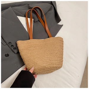 Detail of hand-woven straw tote bag featuring brown leather straps and horizontal texture